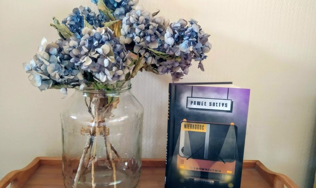 Bukiet kwiatów w słoju a obok książka Pawła Sołtysa "Nieradość"