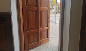 zdjęcie wejścia do budynku biblioteki od wewnątrz.Brązowe drzwi uchylone lekko, w tle widać ulicę