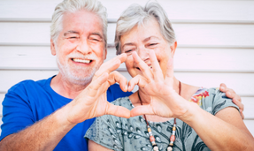 Na zdjęciu dwoje ludzi. Seniorzy łączą swoje dłonie w kształt serca.